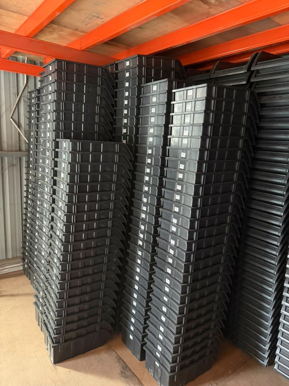 High stacks of black plastic storage bins neatly arranged inside a warehouse facility
