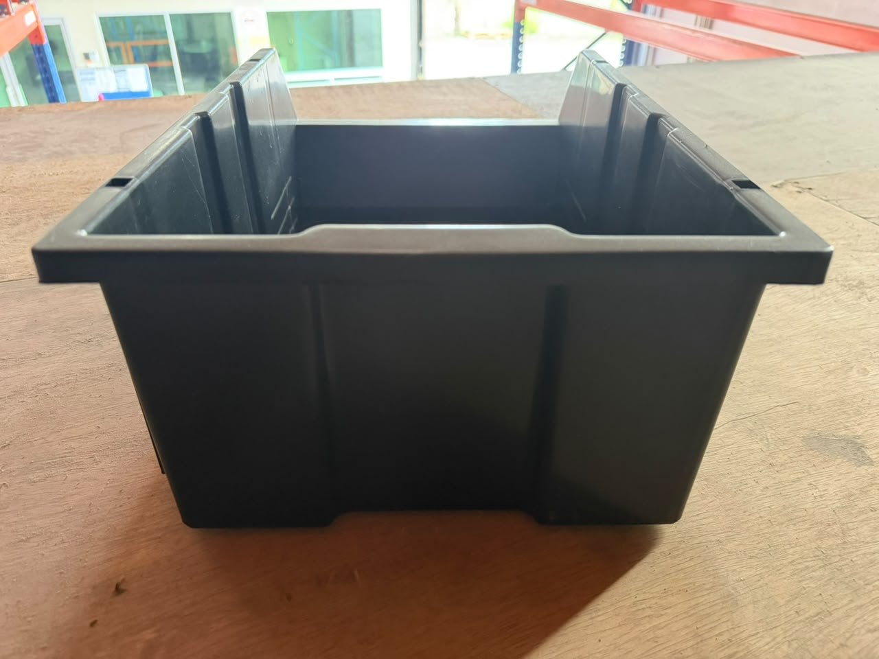 Black polypropylene plastic parts bin viewed from the side on a wooden surface.
