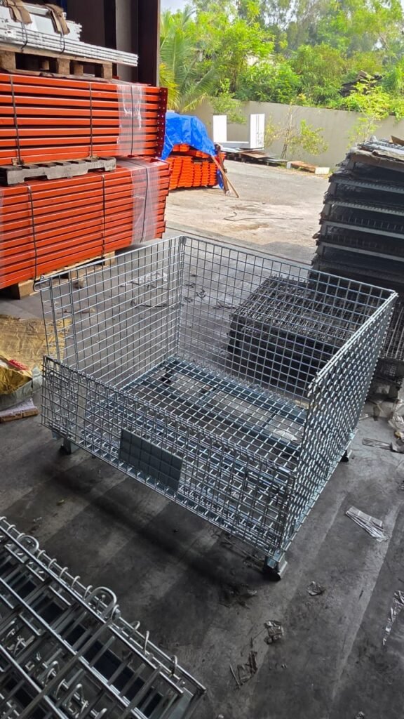 Assembled galvanized wire mesh storage cage with caster wheels in an industrial warehouse.